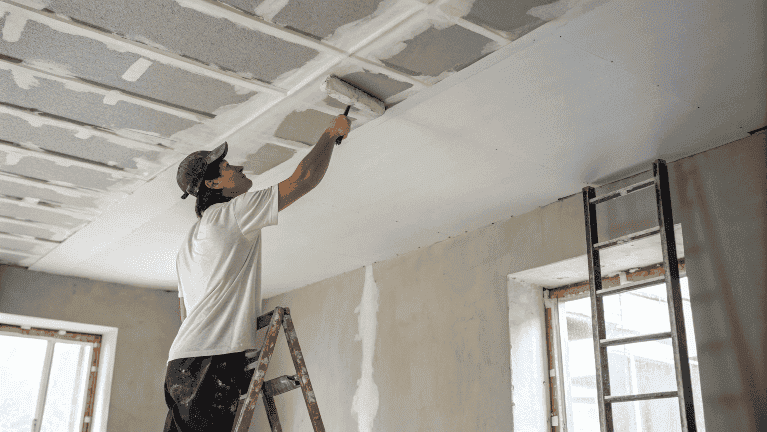 A professional plasterer applying gypsum plaster to a ceiling with a trowel.