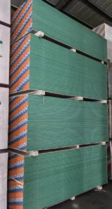 Large stack of green drywall panels in a warehouse, neatly organized with wooden supports separating the piles.