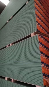 Large stack of green drywall sheets with visible orange branding in a warehouse setting.