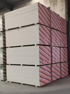 Large stacks of gypsum boards with red and blue patterned edges in a warehouse setting.