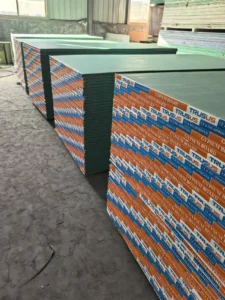 Multiple stacks of gypsum boards neatly arranged inside a factory setting with industrial lighting.