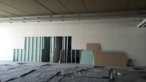 Interior construction site showing unfinished drywall installation and various building materials on the floor.