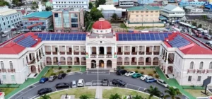 Aerial view of a large historic building with a red roof and solar panels, surrounded by urban landscape and parked cars.
