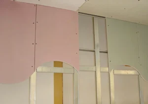View of colorful drywall panels in pink and green mounted on a metal framework, showcasing an interior construction scene.