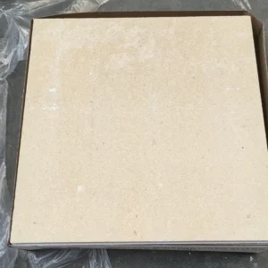 Close-up of a beige tile placed on a concrete surface with plastic wrapping visible.