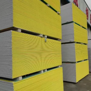 Stacks of yellow and gray drywall panels arranged neatly on pallets in an industrial warehouse setting.